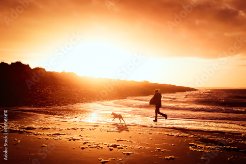 Des Menschen bester Freund - Hund und Mensch laufen gemeinsam in den Sonnenuntergang am Strand © Kim