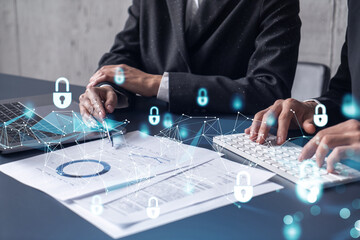 Two businesspeople man and woman working on the project to protect cyber security of international company. Padlock Hologram icons over the table with documents. Formal wear. Workspace.