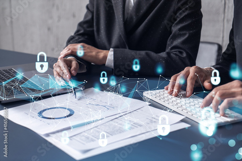 Two businesspeople man and woman working on the project to protect cyber security of international company. Padlock Hologram icons over the table with documents. Formal wear. Workspace.