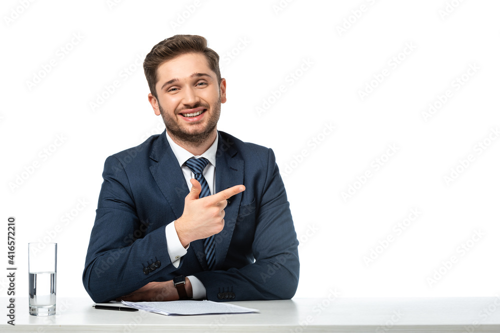 happy anchorman pointing aside with finger near papers and glass of water isolated on white happy anchorman pointing aside with finger near papers and glass of water isolated on white
