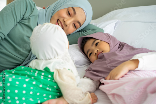 Asian Muslim baby girl with mother and sister wearing HIJAB sleeping on bed
