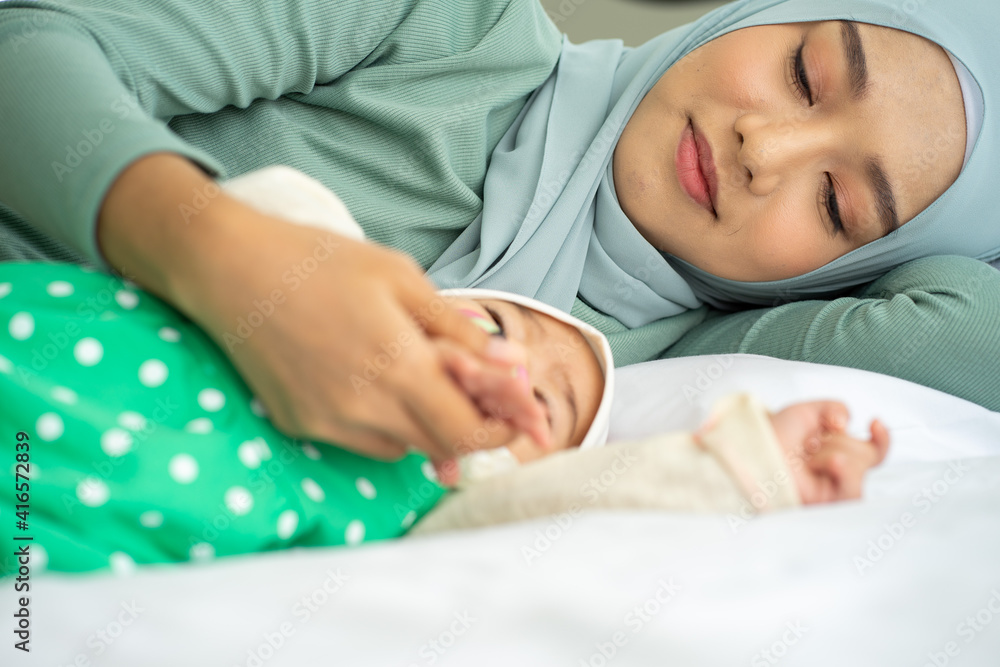 Asian Muslim new born baby wearing HIJAB with mother sleeping on white bed Asian Muslim new born baby wearing HIJAB with mother sleeping on white bed