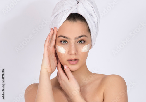 Girl model with face cream under her eyes, concept of skin care and skin products, on white background with copy space