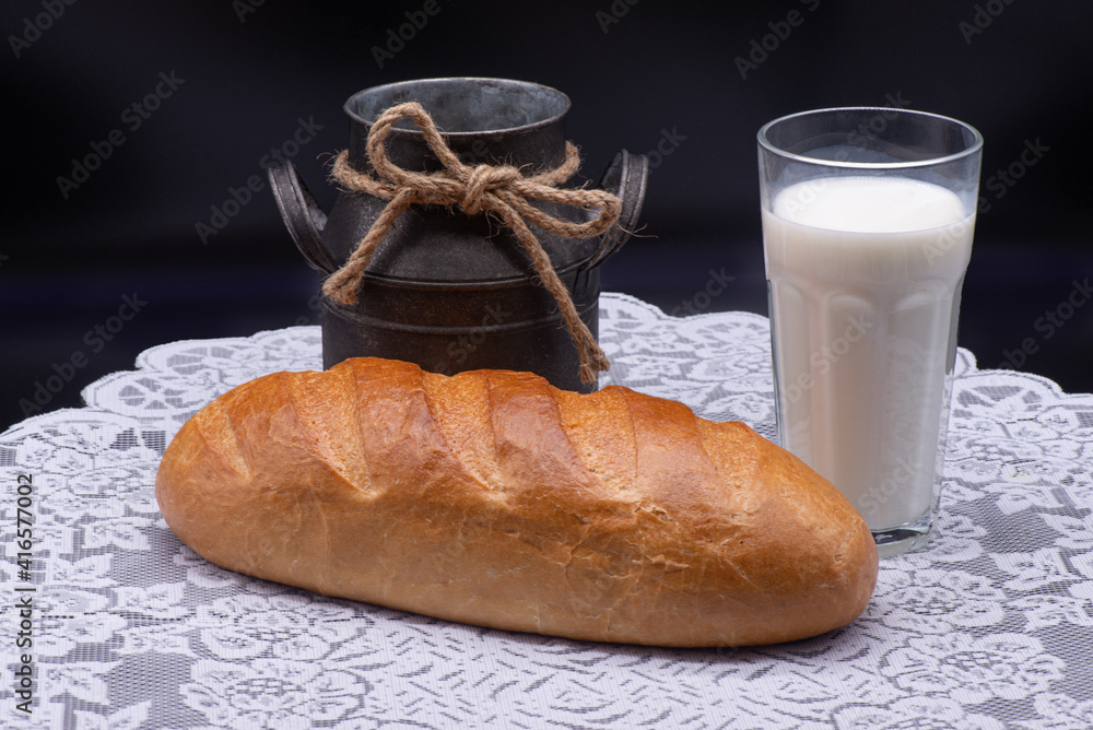 Composition of white bread, glass of milk and old jug on white tablecloth on black background