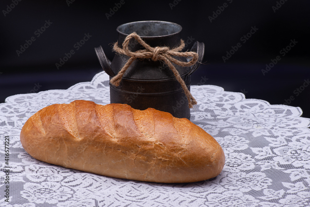 Composition of white bread and old jug on white tablecloth on black background