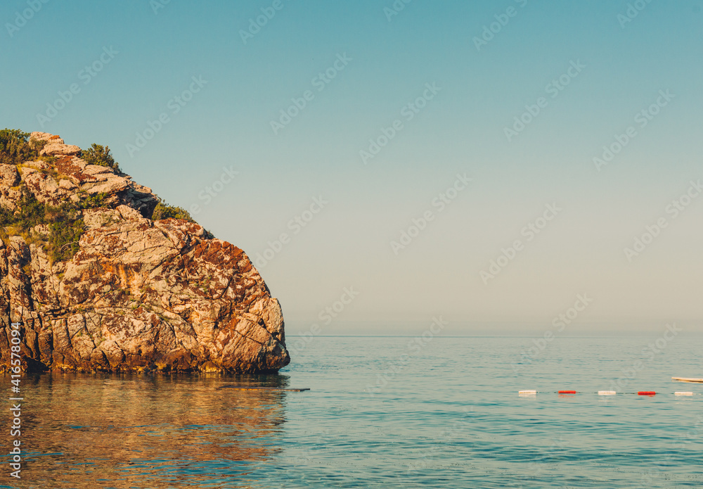 Sunny day at sea with rock on the side. Colorful view on sea and cliff in the water.