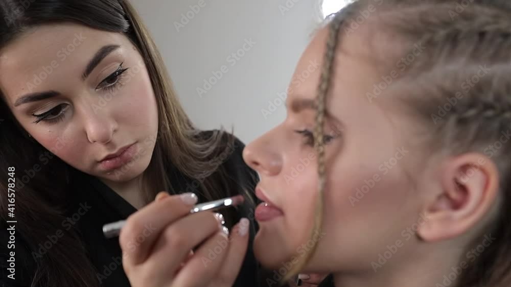 Makeup artist applies nude lipstick. Hand of make-up master, painting lips of young beauty blond hair model. Make up in process. Closeup view Makeup artist applies nude lipstick. Hand of make-up master, painting lips of young beauty blond hair model. Make up in process. Closeup view