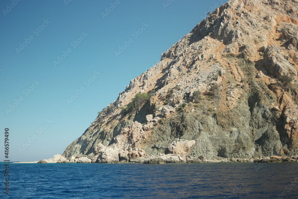 Fototapeta premium Dark blue sea and big stone formation in the background. Cliff over sea surface under blue sky.