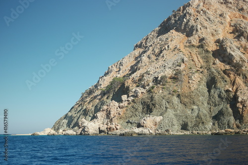 Dark blue sea and big stone formation in the background. Cliff over sea surface under blue sky.