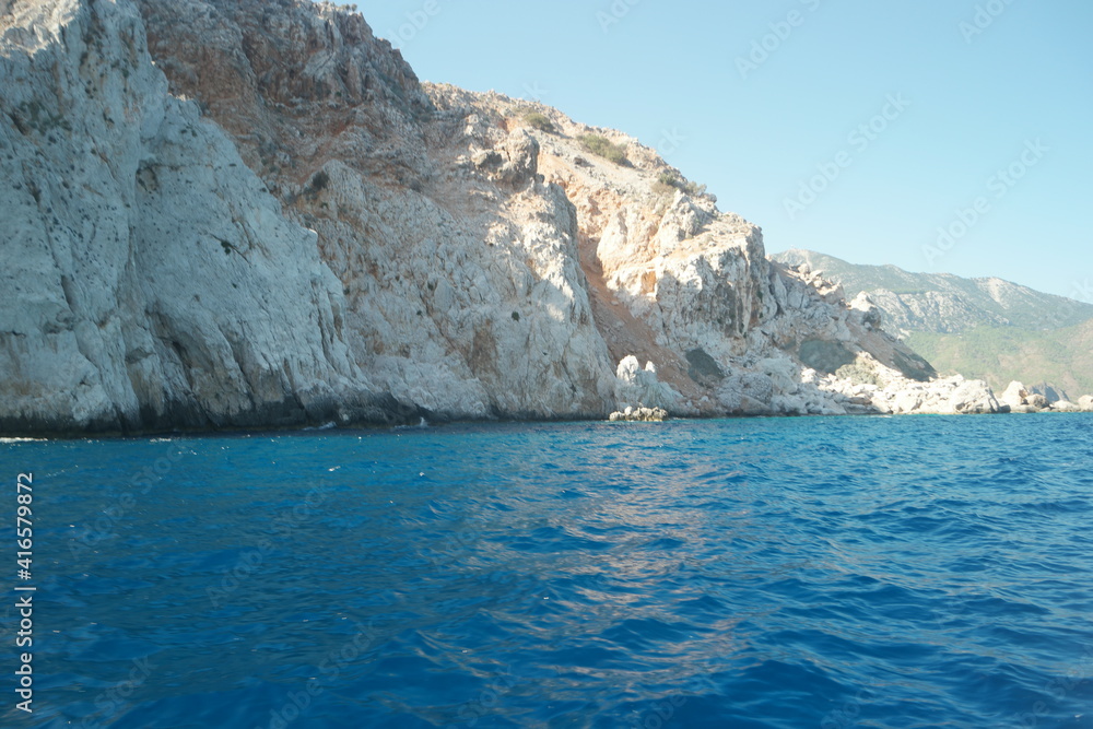Turquoise water in the Mediterranean sea. Rocky cliff in the clear sea water. Calm waves wash huge rocks.