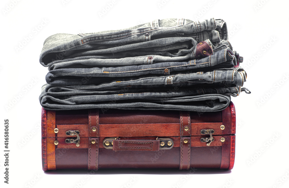 Stack of gray jeans on a brown retro suitcase on white background