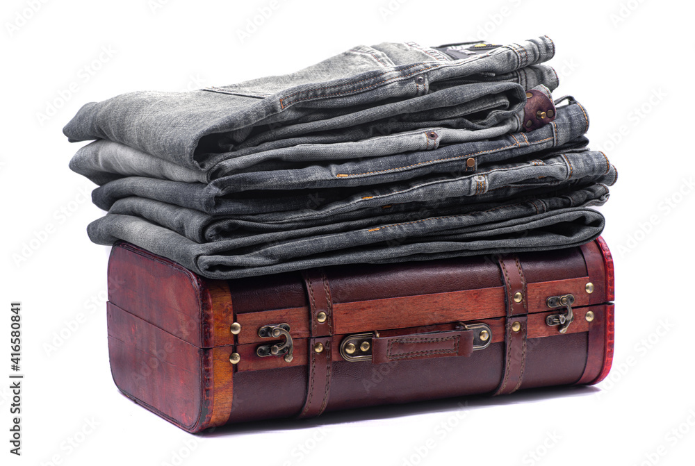 Stack of gray jeans on a brown retro suitcase on white background