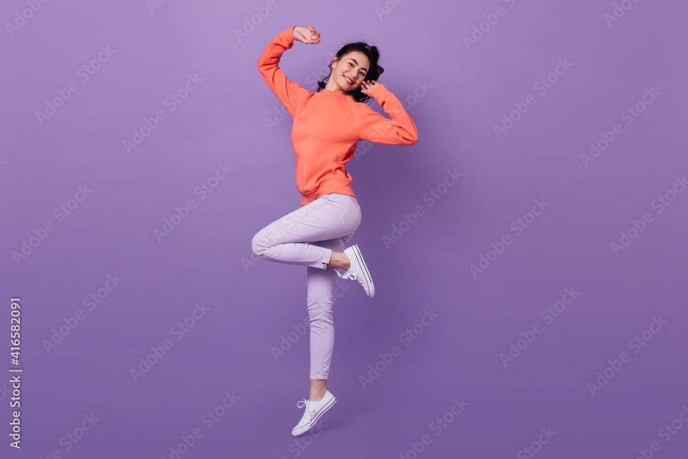 Lovely asian girl standing on one leg. Full length view of attractive stylish japanese woman jumping on purple background.