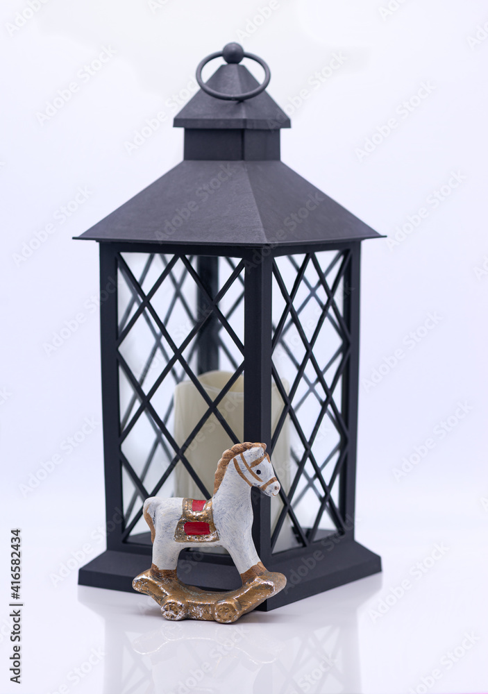 Glass lamp with a candle inside and toy clay horse on a white background