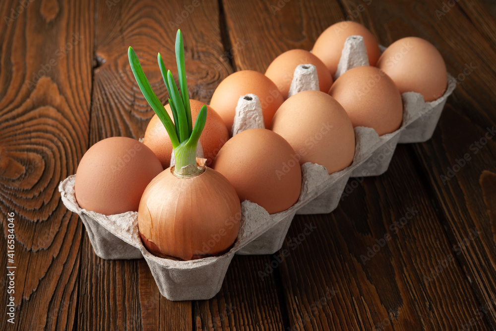 Chicken eggs and green onions. Top view of green onions and brown raw eggs in an egg box on a wooden background. The concept of dietary and healthy natural protein products. Chicken eggs and green onions. Top view of green onions and brown raw eggs in an egg box on a wooden background. The concept of dietary and healthy natural protein products.