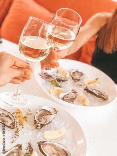 Oysters on the plate on ice with lemon and two glasses of wine next to it.