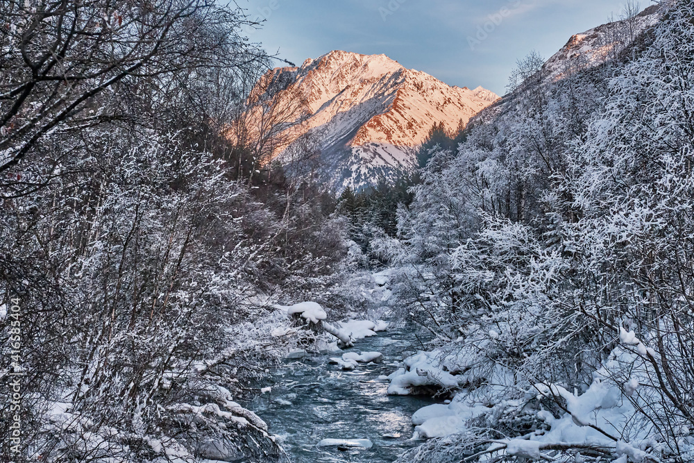 A mountain river running in a snow-covered forest on sunset. Elbrus region, Russia. A mountain river running in a snow-covered forest on sunset. Elbrus region, Russia.
