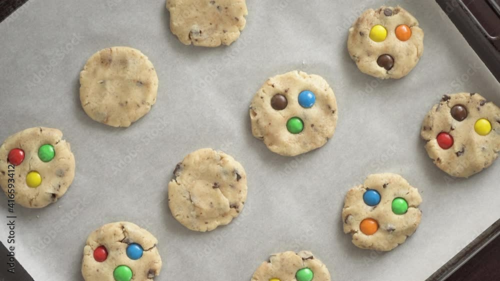 A woman decorates a raw cookie on a baking sheet with colorful M&Ms candies A woman decorates a raw cookie on a baking sheet with colorful M&Ms candies