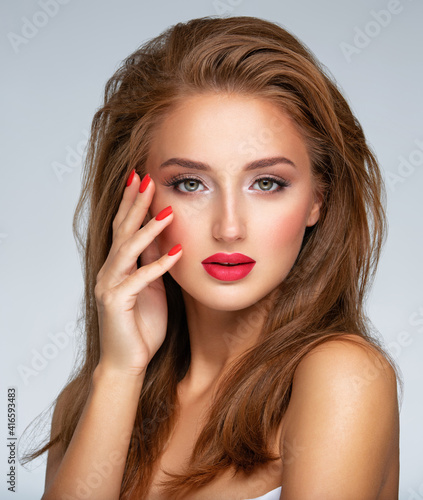 Face of young woman with red nails, lipstick and long brown hair. Model with fashion makeup.