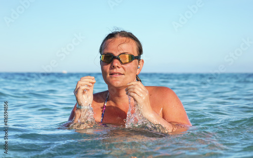 Young woman with swim goggles, surrounded by sea, closeup detail, clear sky background © Lubo Ivanko