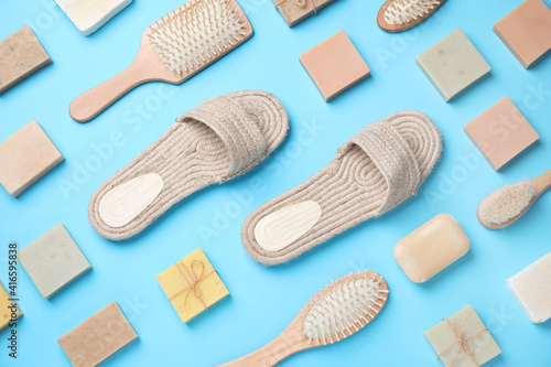 Slippers, hair brushes and soap bars on light blue background, flat lay