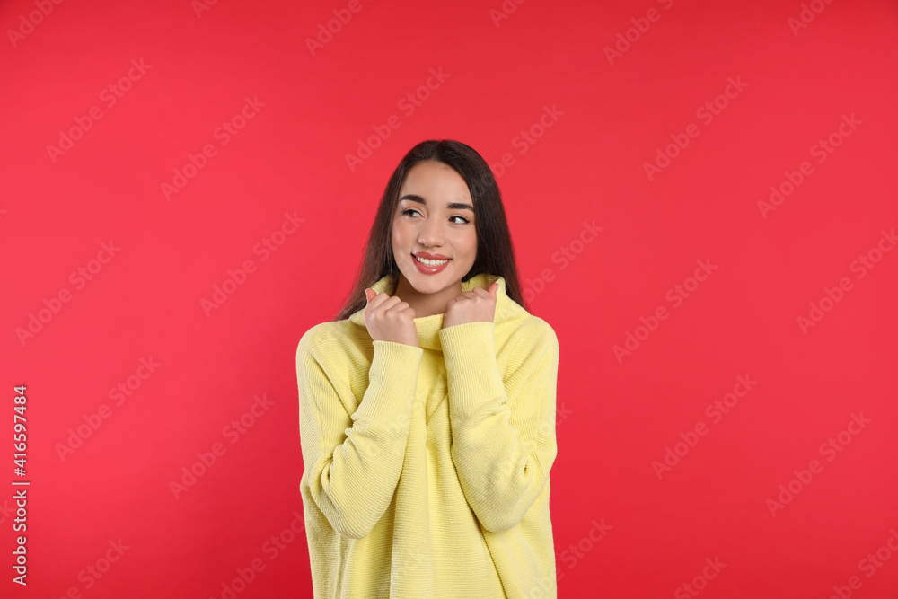 Beautiful young woman wearing yellow warm sweater on red background Beautiful young woman wearing yellow warm sweater on red background