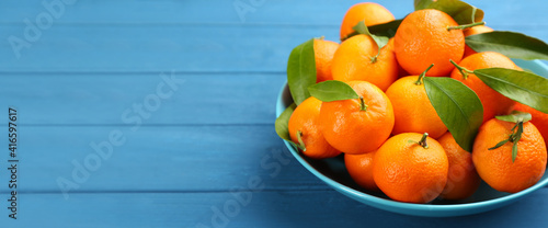 Fresh ripe tangerines with green leaves on blue wooden table, closeup