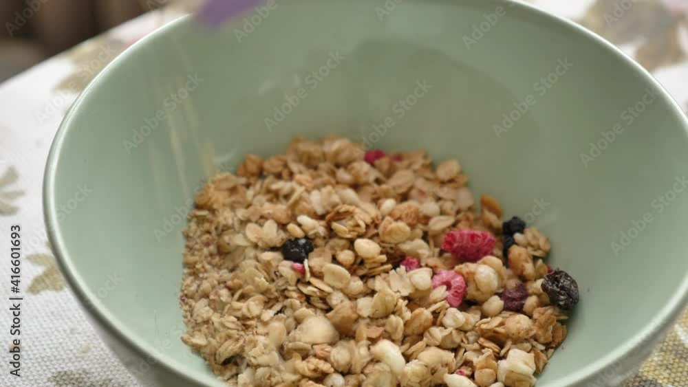 A man pours muesli with pieces of fruit and berries from a bag into a plate in the morning close-up. A rich and healthy breakfast, healthy food and an active lifestyle. A man pours muesli with pieces of fruit and berries from a bag into a plate in the morning close-up. A rich and healthy breakfast, healthy food and an active lifestyle.