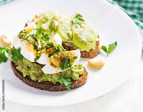 Vegetarian breakfast. Sandwich with avocado puree, boiled eggs and sandwich cream cheese, kiwi, nuts.  Healthy breakfast or lunch.