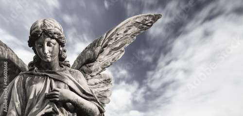 Slika na platnu Sad guardian angel sculpture with open wings isolated with blurred white clouds dramatic sky