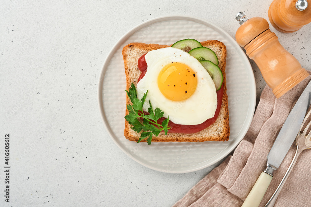 Toast with tomatoes ketchup, cucumber and fried egg on white plate, top view, grey background, Toast with tomatoes ketchup, cucumber and fried egg on white plate, top view, grey background,