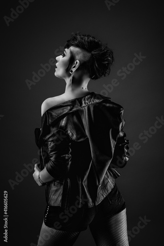 Pretty young woman from back with punk hairstyle, showing off her shoulder, wearing leather jacket and fishnet stockings © Warpedgalerie
