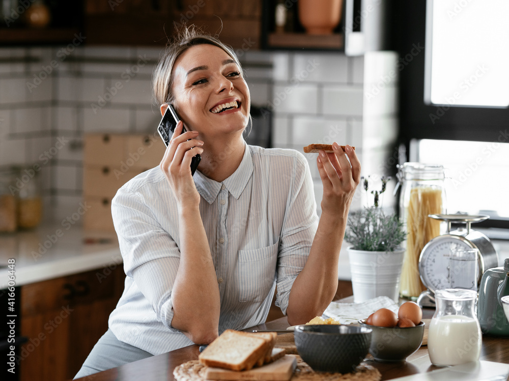 Beautiful woman eaitng sandwich and using the phone in the kitchen. Happy woman talking to the phone Beautiful woman eaitng sandwich and using the phone in the kitchen. Happy woman talking to the phone