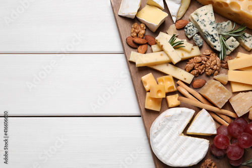 Cheese plate with grapes and nuts on white wooden table, top view. Space for text
