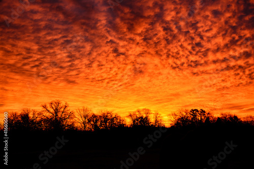 Dramatic morning sky before sunrise, with yellow and orange hues against silhouetted trees in rural landscape