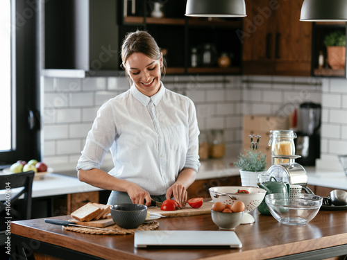 Young woman is reading a recipe while cooking. Beautiful woman using laptop in the kitchen. Healthy food.