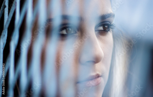 Close-up portrait of beautiful teen brunette girl. View through the metal wire