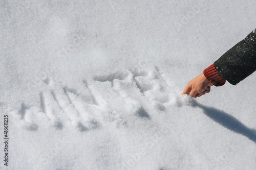 A man in a coat with his hand and forefinger writes, draws letters and the word winter on the white fresh snow. Photography, concept, top view.