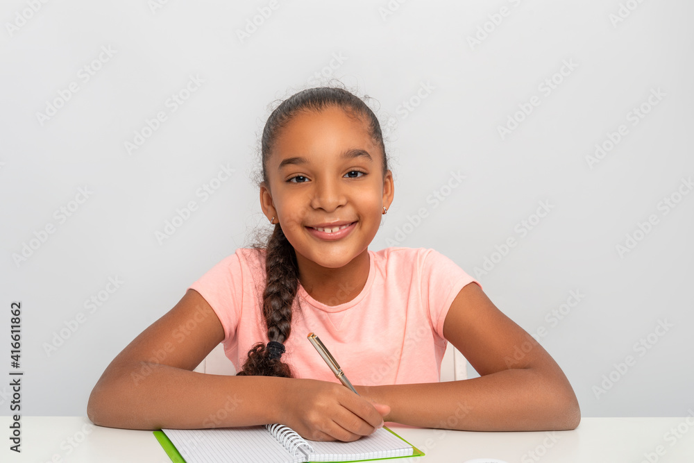 Portrait of the schoolgirl siting at the table indoors and doing her homework Portrait of the schoolgirl siting at the table indoors and doing her homework