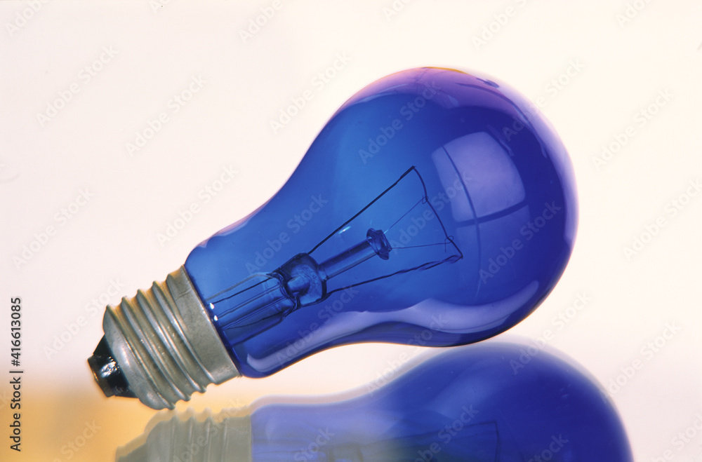 Electric incandescent lamp bulb of blue color on a light background, close-up. Electric incandescent lamp bulb of blue color on a light background, close-up.
