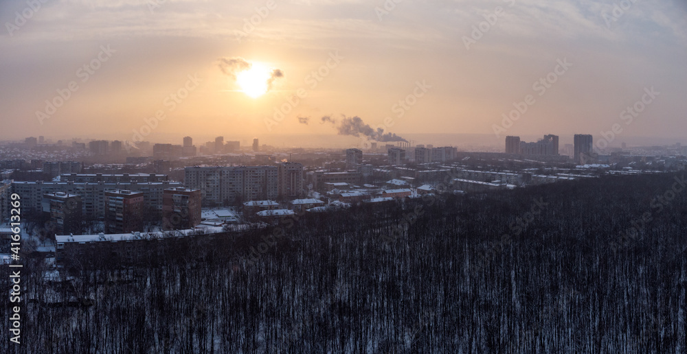 Aerial view Kharkiv city Pavlove Pole district. Smoke from pipes above winter dark forest, multistorey houses and snowy sunset sky