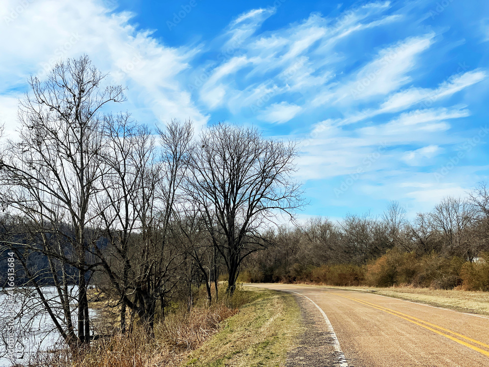 Curving road along a river in winter with dramatic clouds in a blue sky Curving road along a river in winter with dramatic clouds in a blue sky