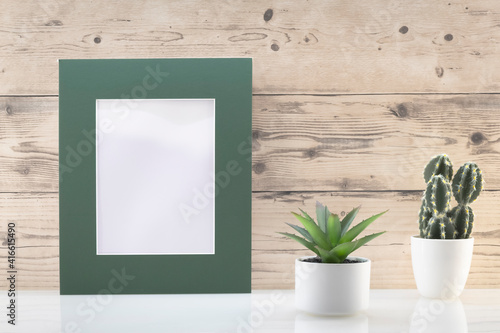 Modèle de cadre photo blanc avec espace vide pour logos, inscription publicitaire. Cadre en mode portrait sur un espace de travail avec des plantes vertes. © ODIN Daniel