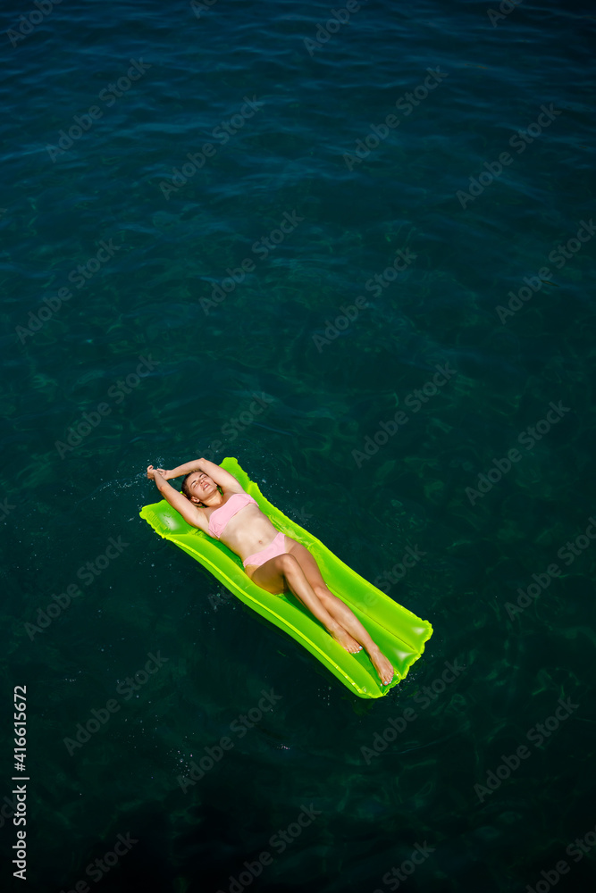 A young woman in a swimsuit swims on an inflatable bright mattress in the sea. Summer vacation concept.