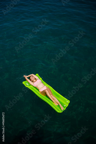 A young woman in a swimsuit swims on an inflatable bright mattress in the sea. Summer vacation concept. © Дмитрий Ткачук