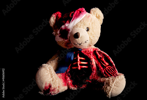 bear on a black background with a broken head. with a bandaged eye. a skeletal hand and a torn belly. halloween concept. horror toy