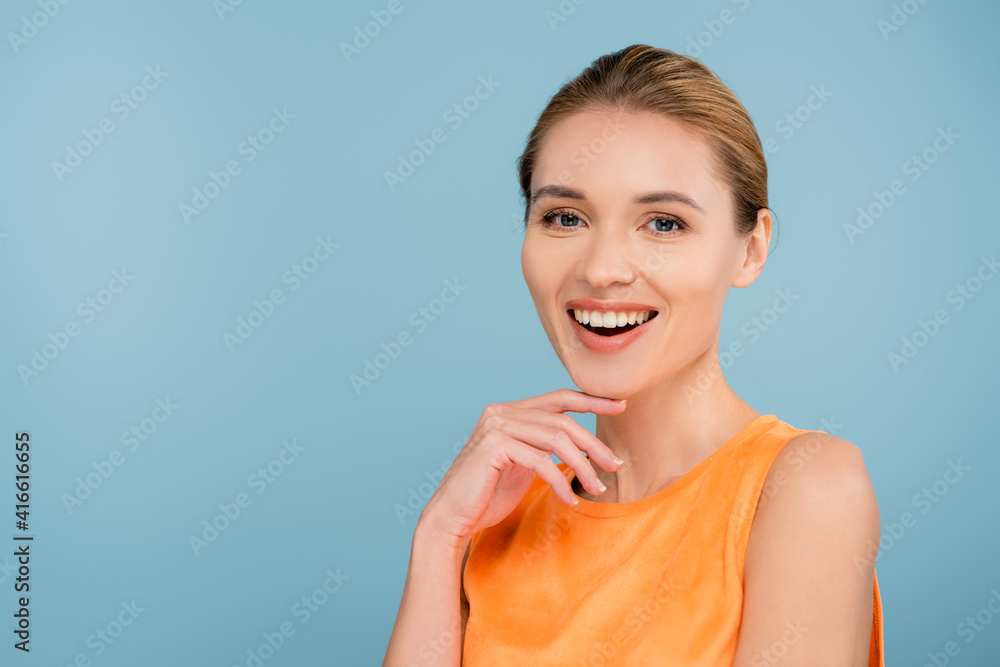 happy woman in orange singlet smiling at camera isolated on blue