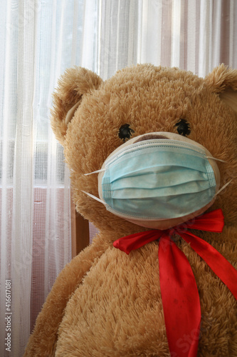 Lockdown Teddy Bear Portrait wearing medical mask from protection of coronavirus covid 19, global pandemic. Self isolation symbolism, sitting by the window, wearing red bow tie.  © Nodi