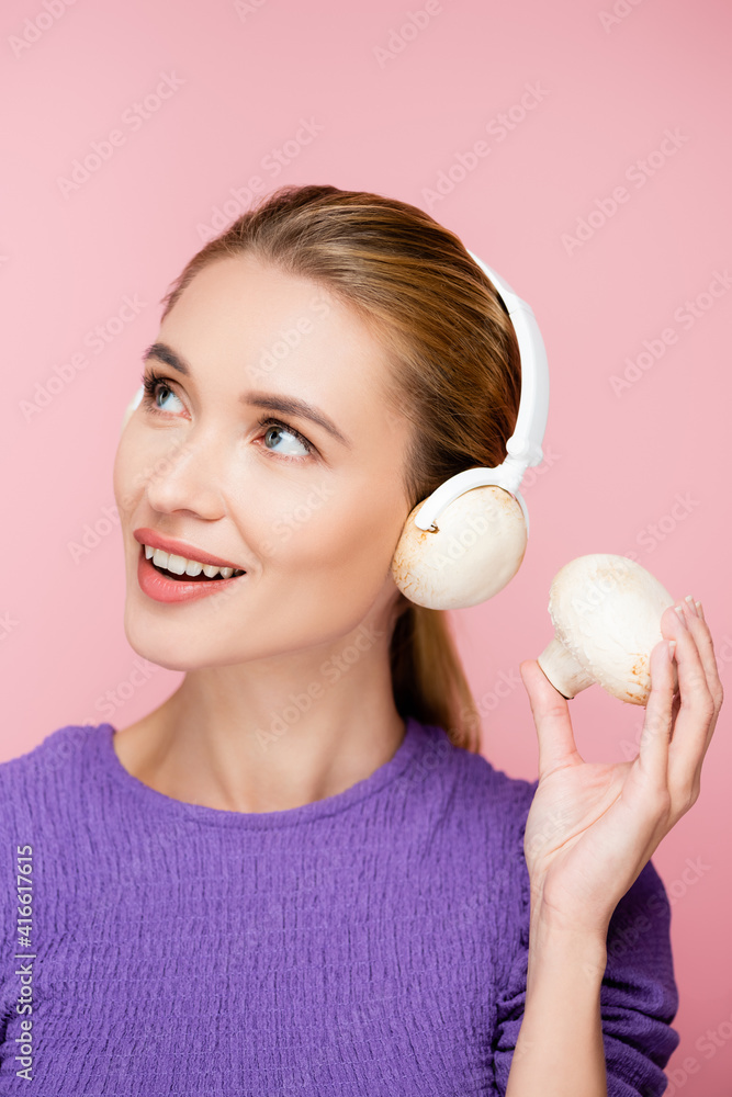 cheerful woman with mushroom in headphones looking away isolated on pink cheerful woman with mushroom in headphones looking away isolated on pink