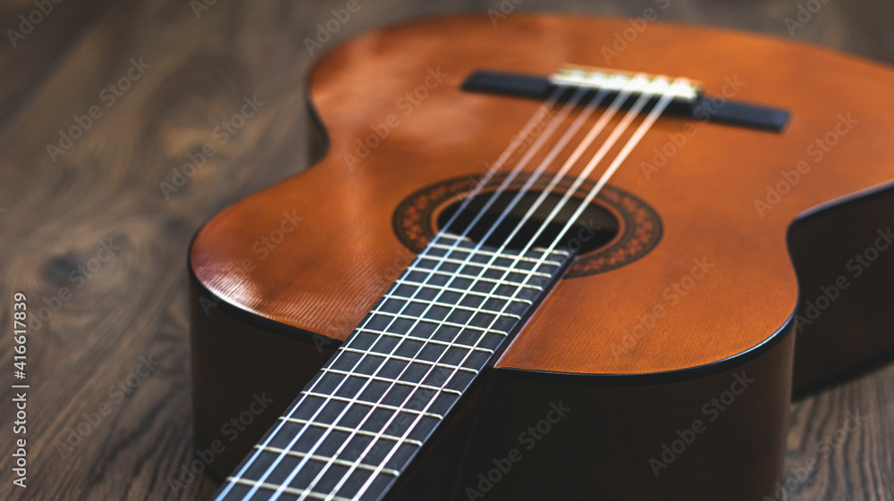 Fototapeta premium Wooden guitar on a wooden background, close-up, strings. Musical retro instrument. 